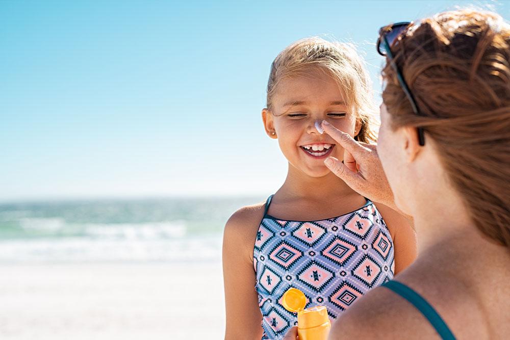 Mutter cremt Kind mit Sonnencreme ein am Strand